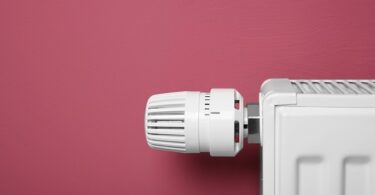 Heating radiator with temperature regulator on pink background, closeup